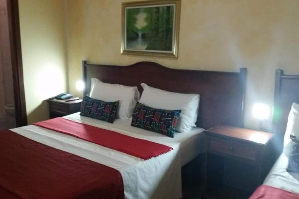 Une chambre d’hôtel avec un grand lit, deux tables de chevet, une tête de lit en bois et un tableau au mur.