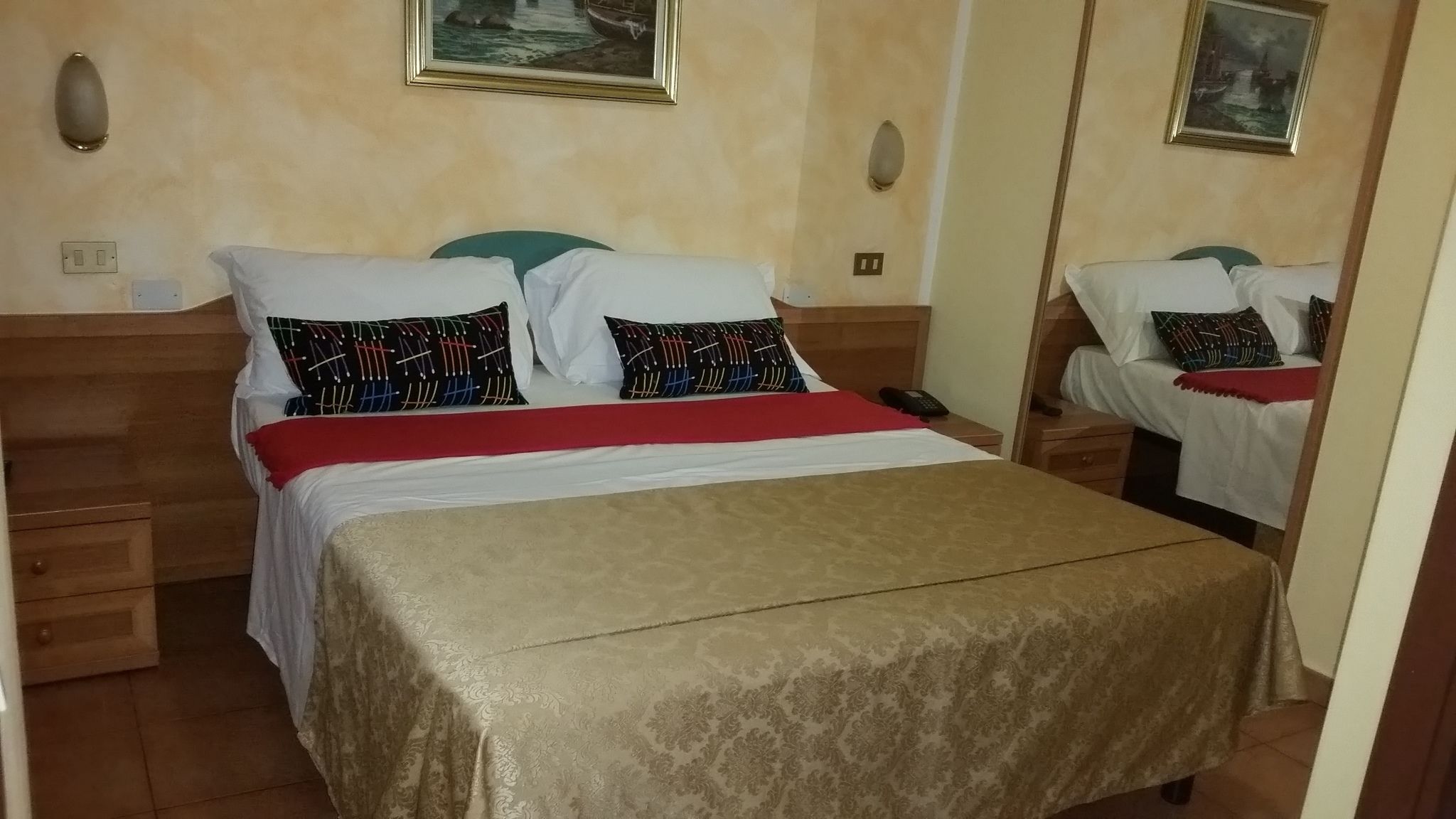 A neatly made bed with patterned pillows, a red blanket, and a wooden headboard.
