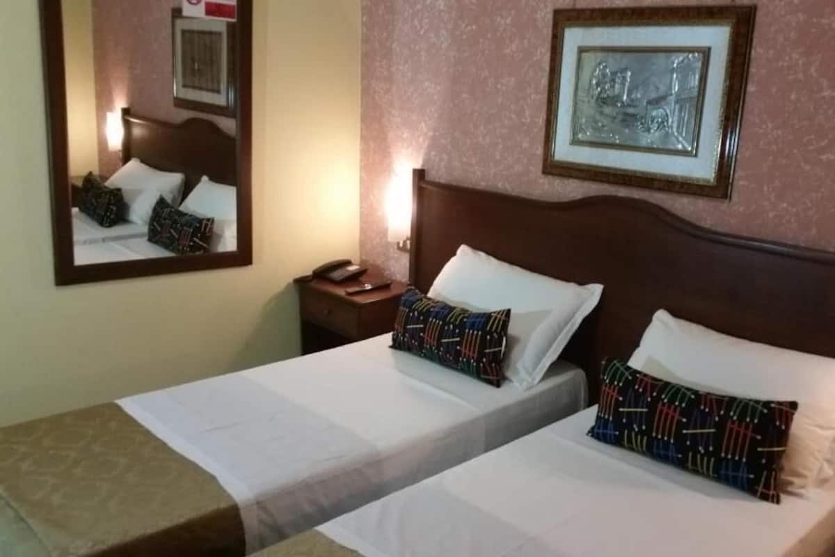 Une chambre d’hôtel avec deux lits, une table de chevet avec un téléphone, un tableau encadré au mur et un miroir qui reflète la pièce.