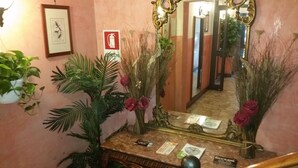 A hallway with a marble floor, a mirror, and a fire extinguisher sign. There are potted plants and a small table with a menu. - Hotel Chopin (Milan)