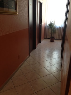 Un pasillo con suelo de baldosas, una planta en maceta y puertas que dan a varias habitaciones.