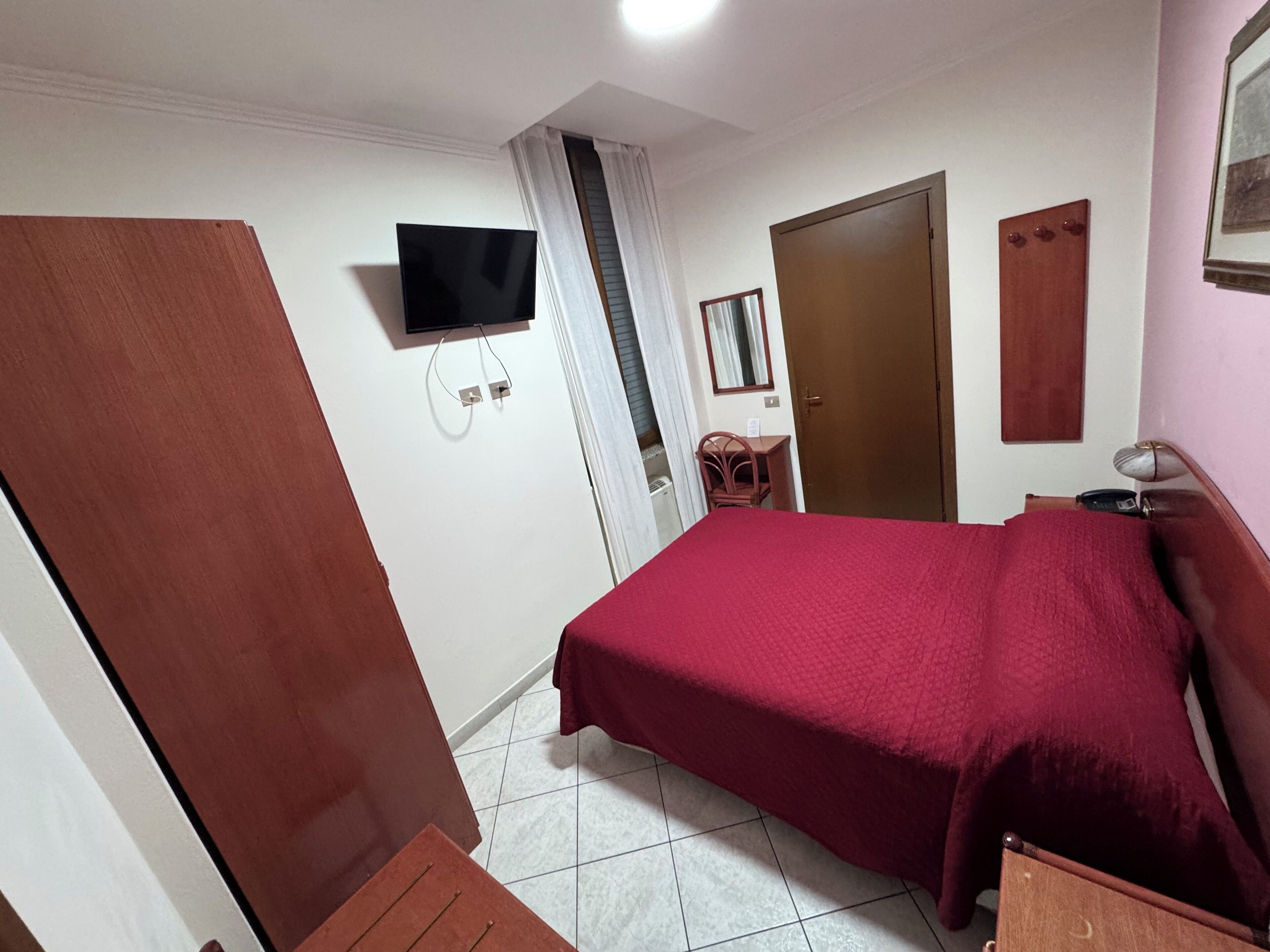 Ein Schlafzimmer mit einem Bett, einem an der Wand befestigten Fernseher, einer Tür und einem Sessel.