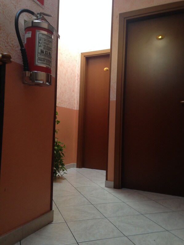A hallway with a fire extinguisher mounted on the wall, a door, and a potted plant. - Hotel La Caravella (Milan)