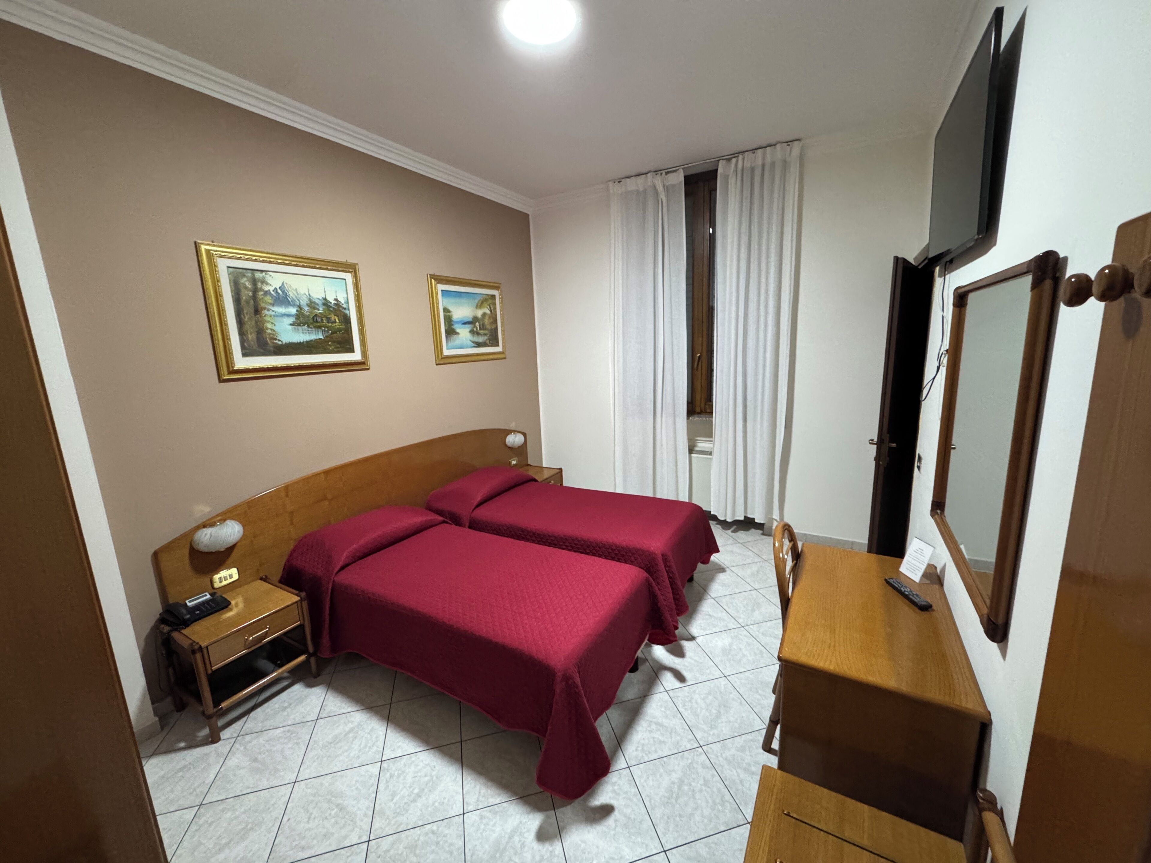 Habitación de hotel con dos camas, un escritorio, una silla, un televisor y dos cuadros en la pared.