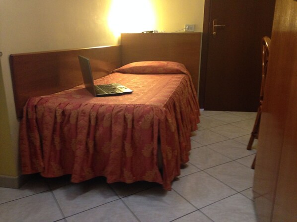 Una habitación pequeña con una cama, un ordenador portátil sobre la cama y una puerta.