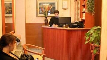 Un'area reception di un hotel con un addetto alla reception alla scrivania, una zona d'attesa con sedie e un pavimento in moquette.