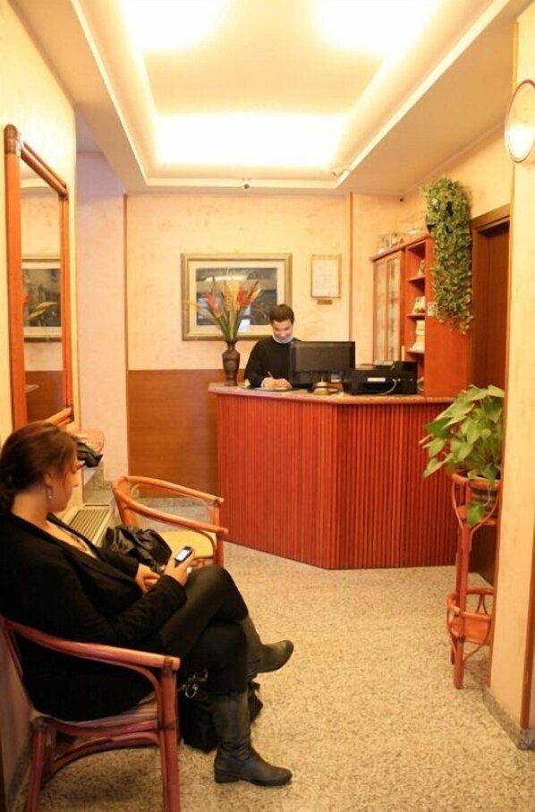 A hotel reception area with a receptionist at the desk, a waiting area with chairs, and a carpeted floor. - Hotel La Caravella (Milan)