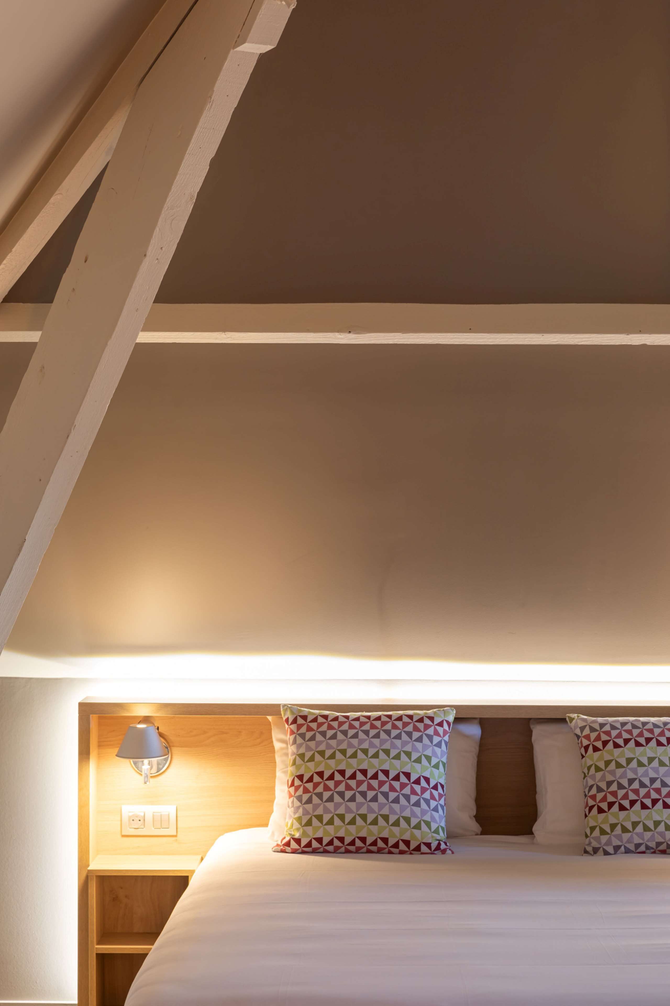 A neatly made bed with patterned pillows, a bedside lamp, and a wooden nightstand.