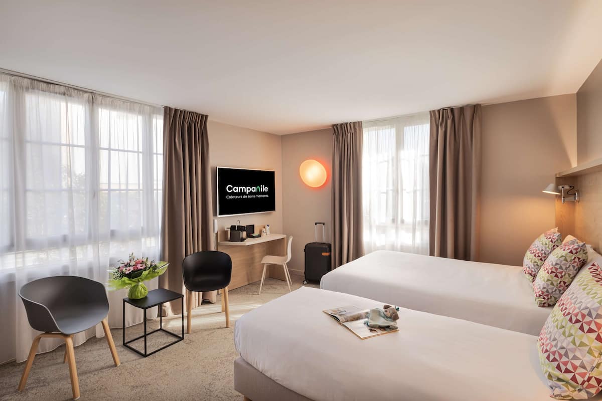Una habitación de hotel con dos camas, un escritorio, una silla, un televisor y una lámpara.