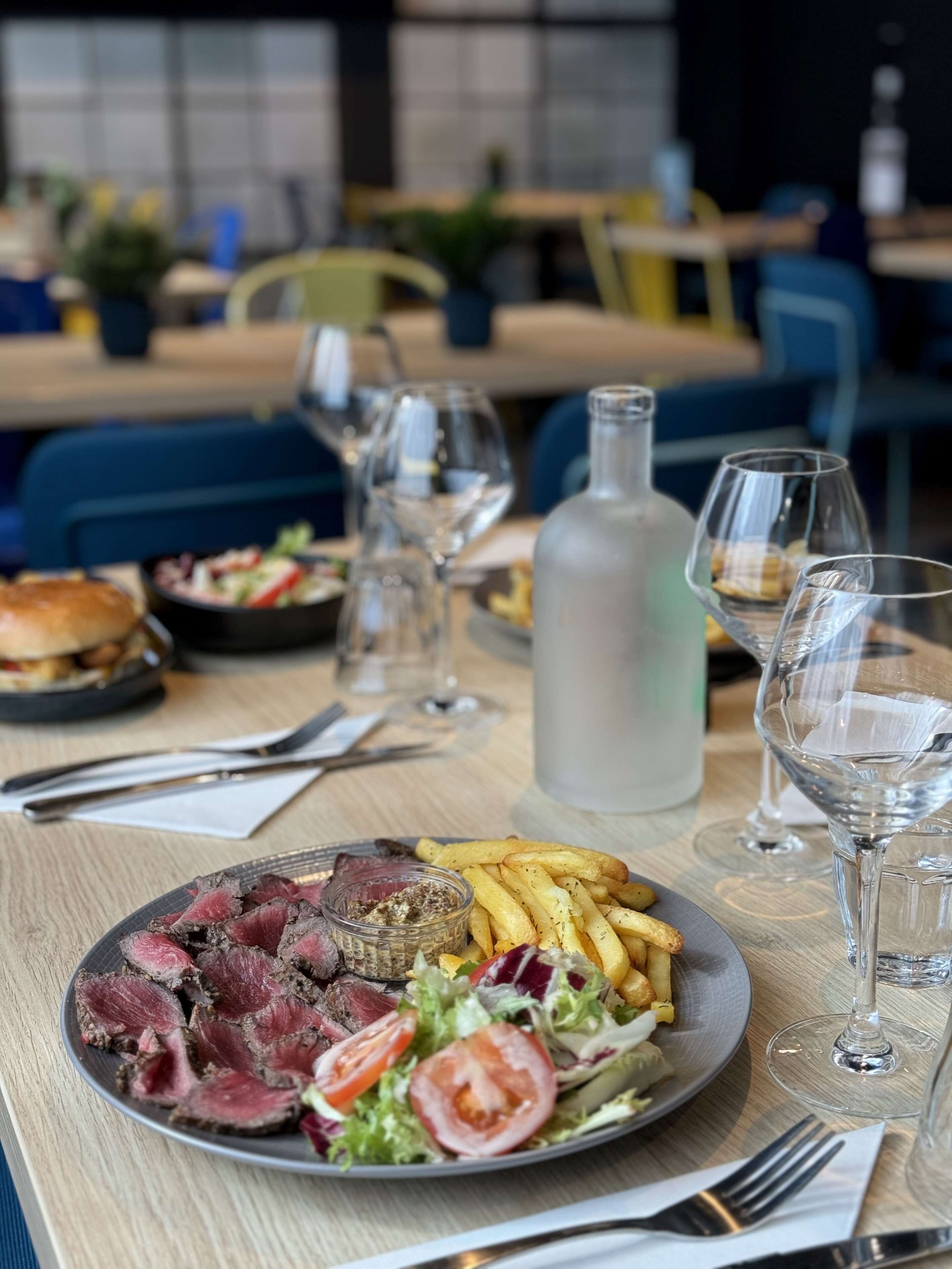 Una mesa de comedor con un plato de comida, copas de vino y una botella de agua.