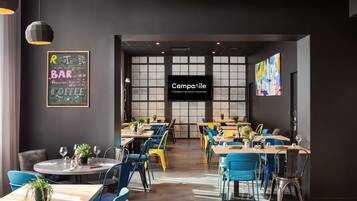 L’intérieur d’un restaurant moderne, avec des tables rondes, des chaises bleues et jaunes, et un menu écrit à la craie sur le mur.