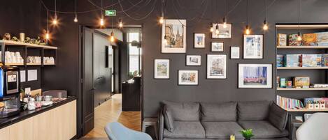 A modern lounge area with a sofa, chairs, a coffee table, and a bookshelf with books and board games.