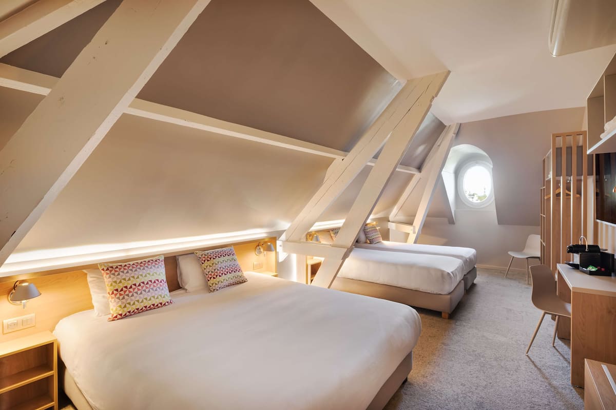 Un dormitorio con una cama grande, una cama más pequeña, un escritorio y una silla. Hay una ventana y un tragaluz.