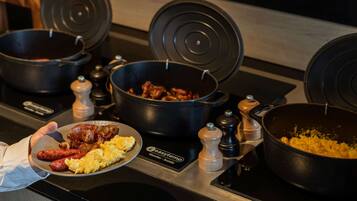A buffet setup with various dishes including sausages, scrambled eggs, and a pot of meat.