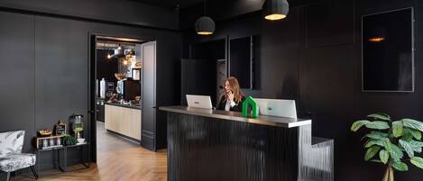 A modern reception area with a dark wood floor, a reception desk with a laptop, and a green house-shaped decoration.