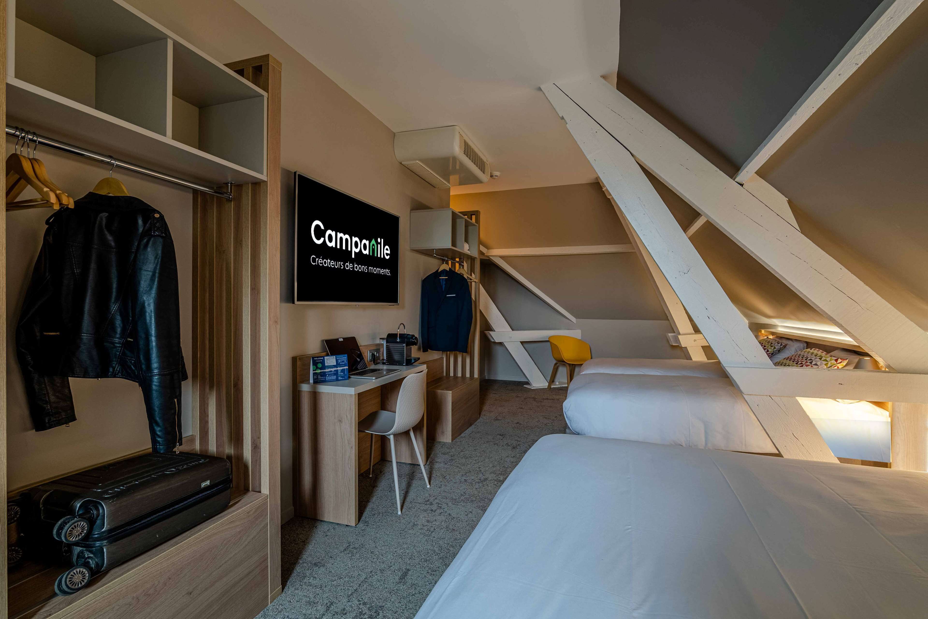 Ein kleines Hotelzimmer mit einem Bett, einem Schreibtisch mit einem Laptop, einem Stuhl, einem Kleiderschrank und einer Treppe.