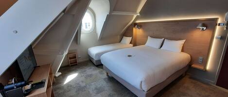 A modern bedroom with a large bed, two smaller beds, a desk with a computer, and a small window.