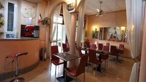A restaurant with red chairs and tables, a coffee machine, and a counter with a menu. - Hotel Piola (Milan)