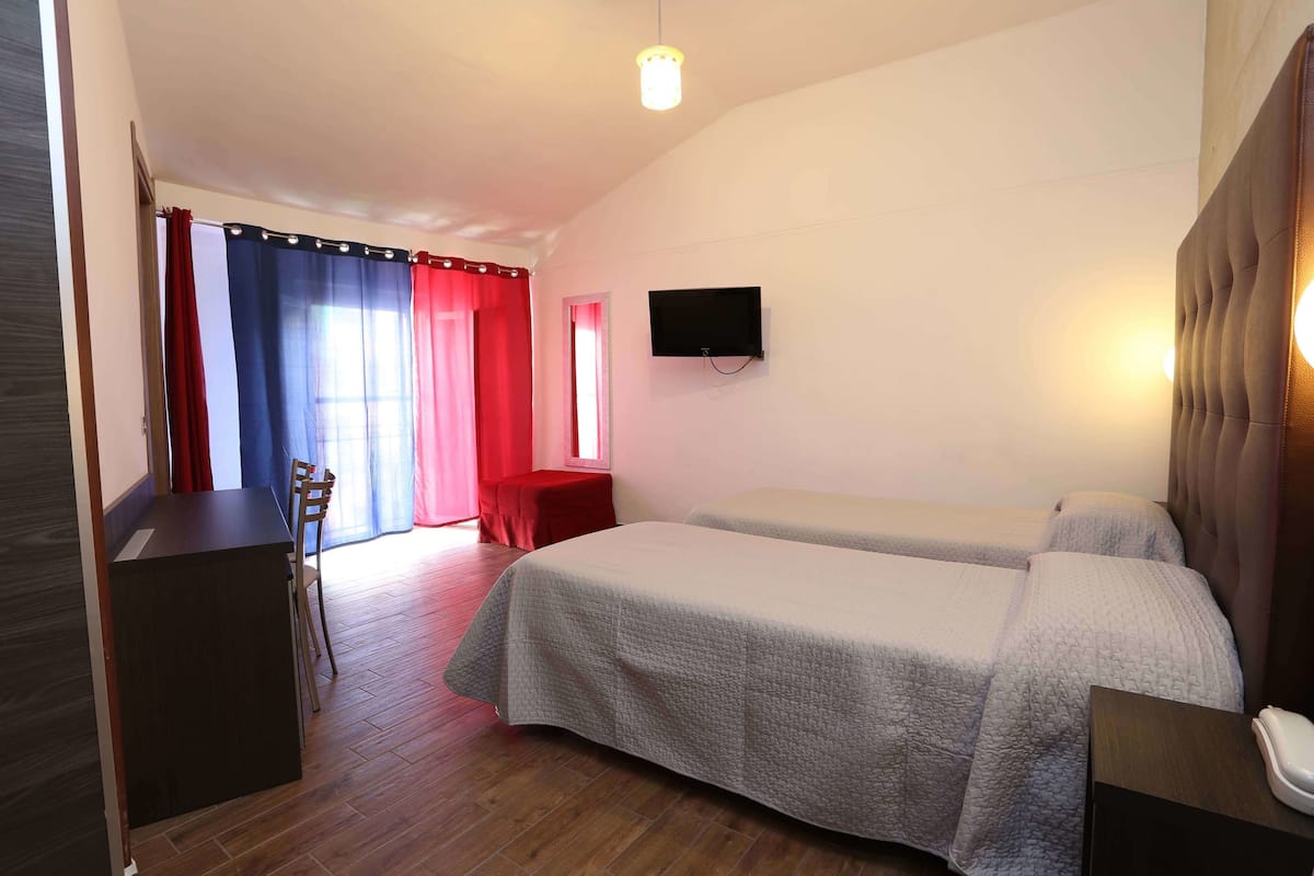 A hotel room with two beds, a desk, a chair, a TV, and a red curtain.