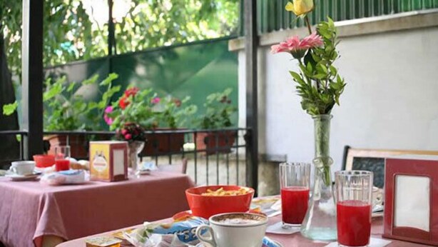 A table set for breakfast with a red tablecloth, a vase with flowers, and a glass of red juice. - Hotel Piola (Milan)