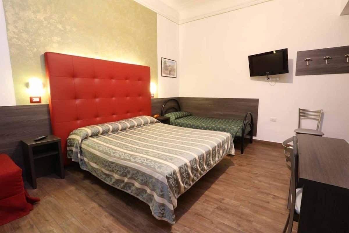 A bedroom with a red headboard, two beds, a TV, a desk, and a chair.