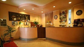 A hotel reception area with a counter, a seating area with a chair, a plant, and a wall-mounted clock. - Hotel Piola (Milan)