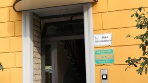 The entrance to El Piala Hotel, featuring a yellow facade, a black and yellow sign, and a staircase leading inside. - Hotel Piola (Milan)