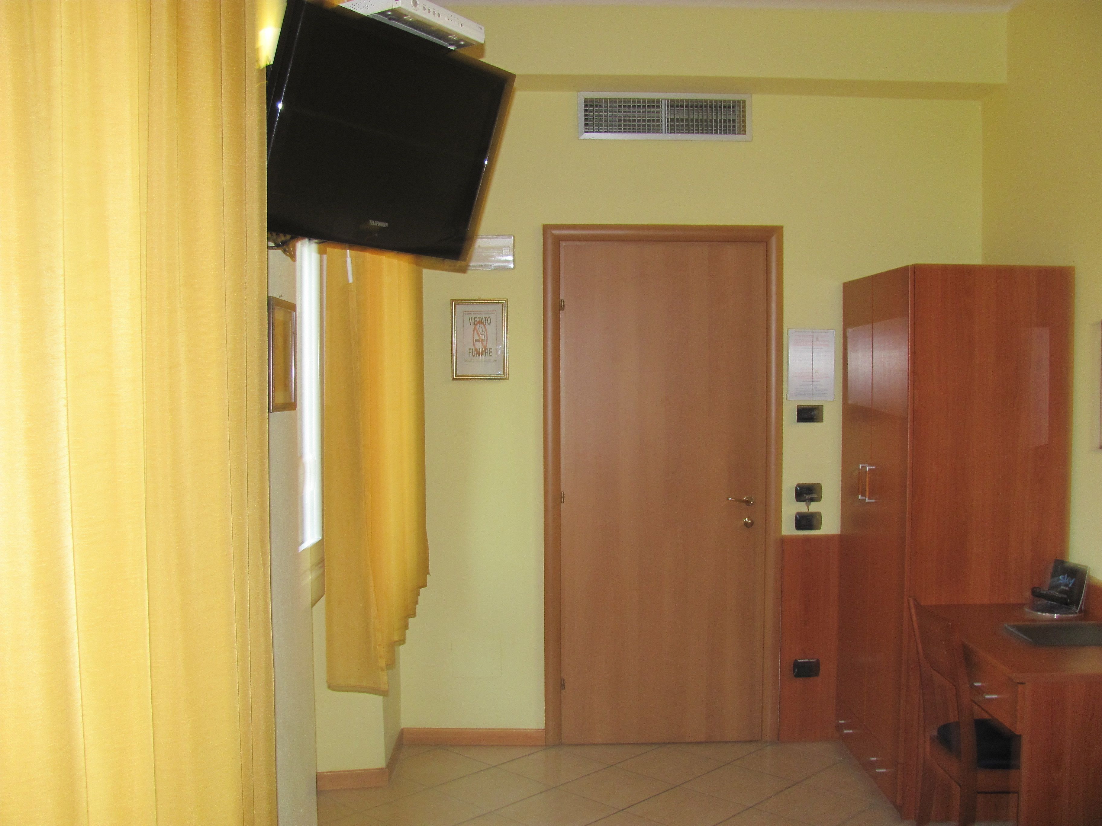Ein Zimmer mit Holzschrank, einer Tür, einem kleinen Tisch mit Stuhl und einem an der Wand befestigten Fernseher.