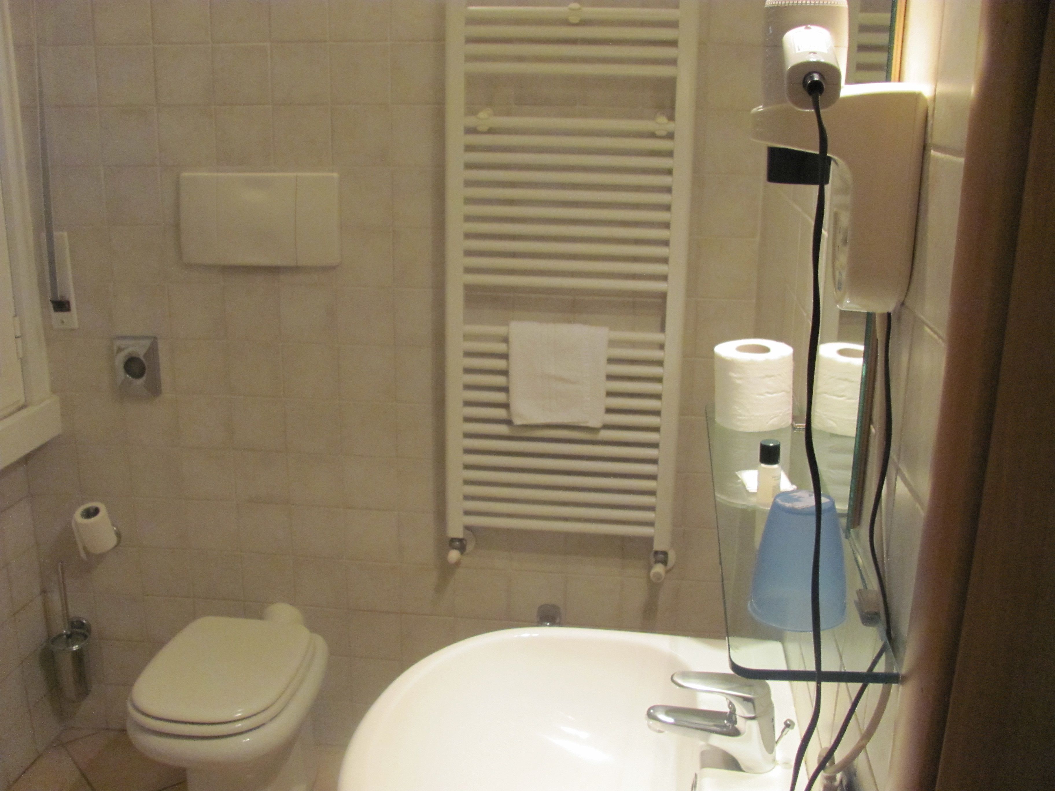 A bathroom with a toilet, sink, towel rack, and toilet paper.