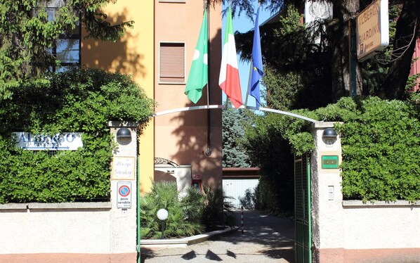 Entrada de un hotel con banderas, un cartel que indica 'Albergo Giardino' y un letrero de 'prohibido estacionar'.