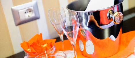 Ein metallischer Eimer mit einem weißen Servietttuch, zwei gläserne Weinkelche und eine kleine Schale mit grünen Oliven auf einem orangen Servietttuch.
