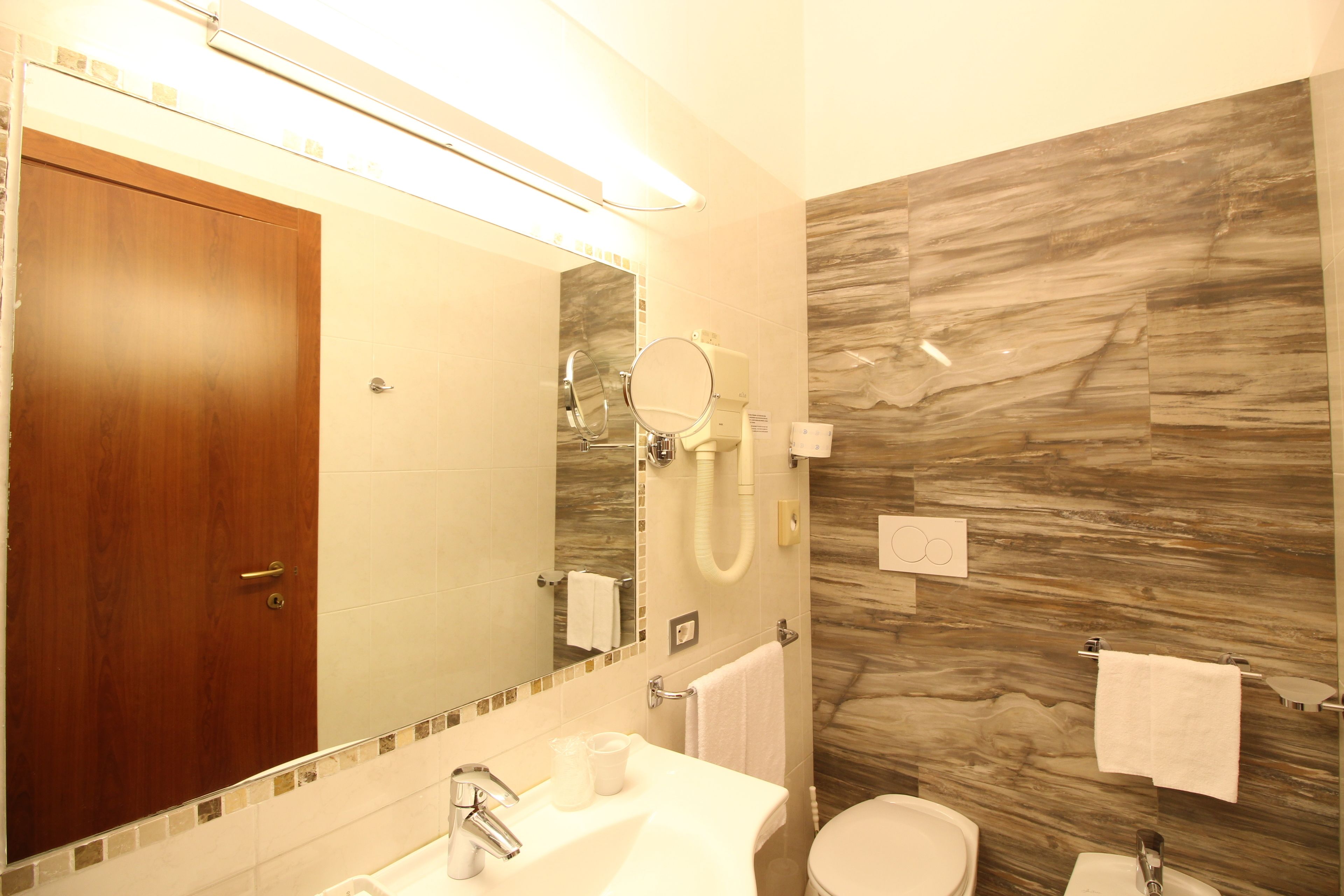 A bathroom with a wooden door, a mirror, a sink, a toilet, and a towel rack.