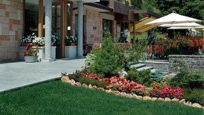 Un edificio moderno con fachada de piedra, un acceso cubierto y un jardín ajardinado con flores coloridas y un pequeño árbol.