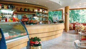 Un vestíbulo de hotel con un mostrador de recepción curvo, una vitrina de vidrio y una zona de estar con mesas y sillas.