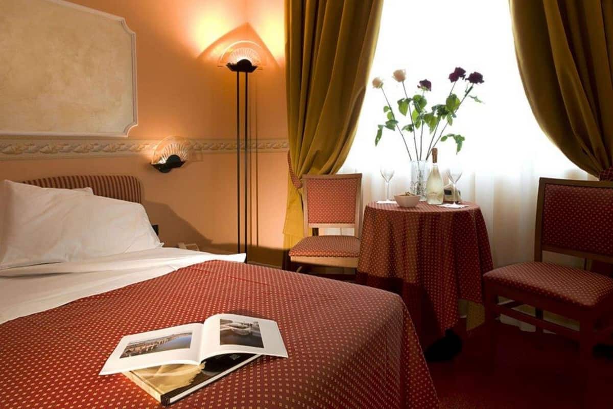 Een hotelkamer met een bed, twee stoelen, een tafeltje met een bloevas en een lamp.