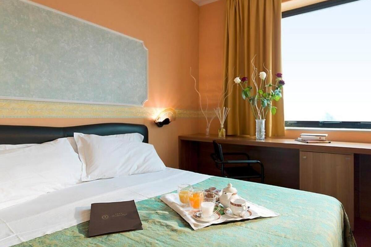 Een hotelkamer met een bed, een bureau met stoel, een vaas met bloemen en een dienblad met ontbijtartikelen.