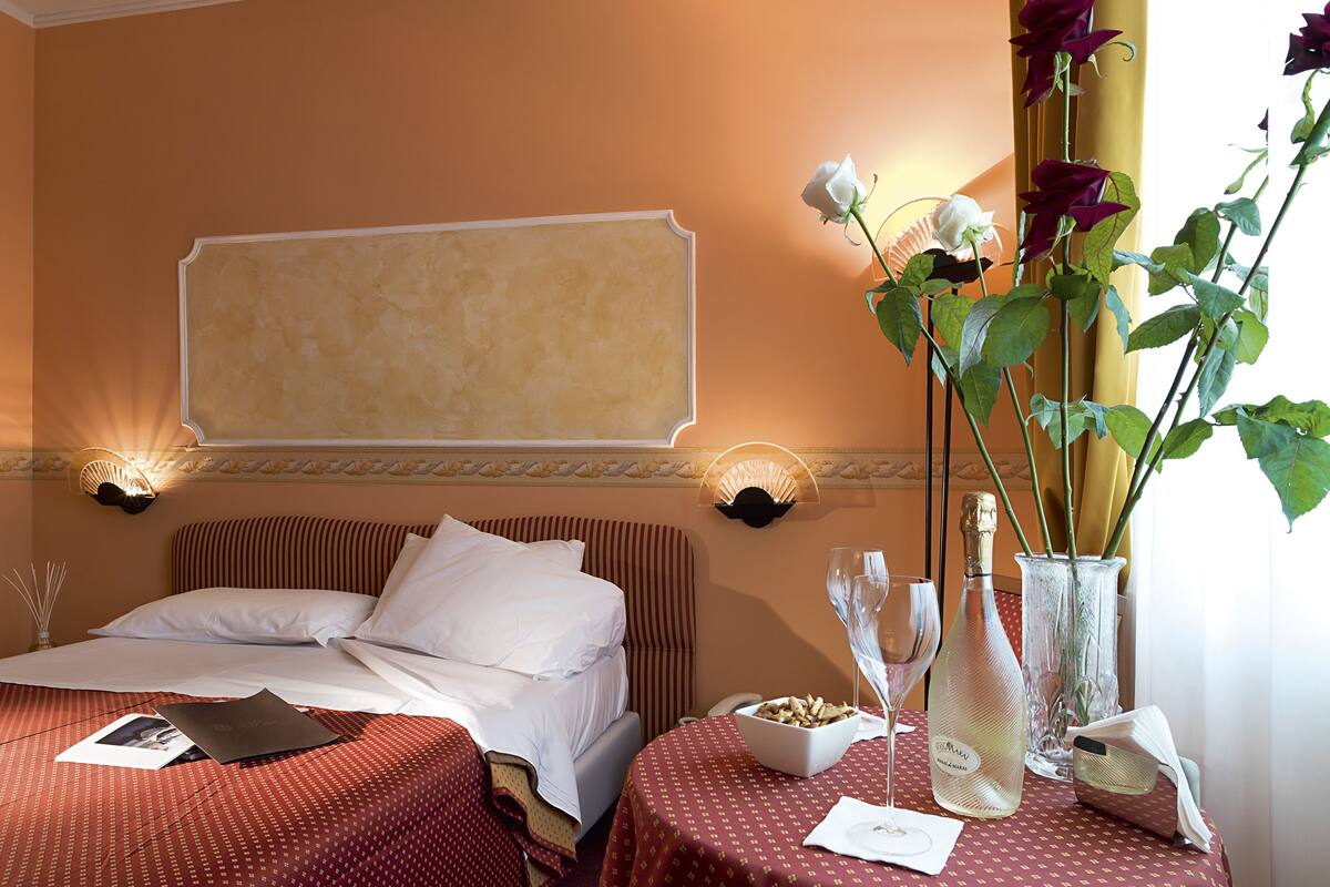 Hotelkamer met twee bedden, een nachtkastje met een bloevas, een fles champagne en een schaal fruit.