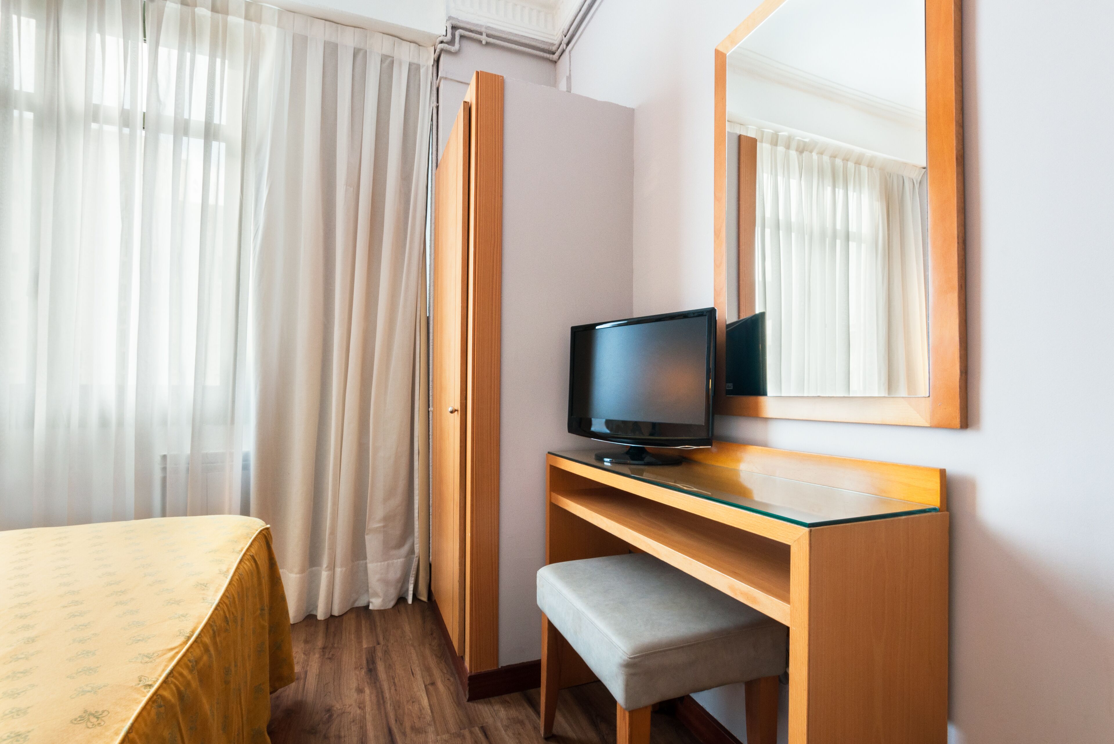 Une chambre d’hôtel avec un lit, un bureau équipé d’un ordinateur, une chaise et un grand miroir.