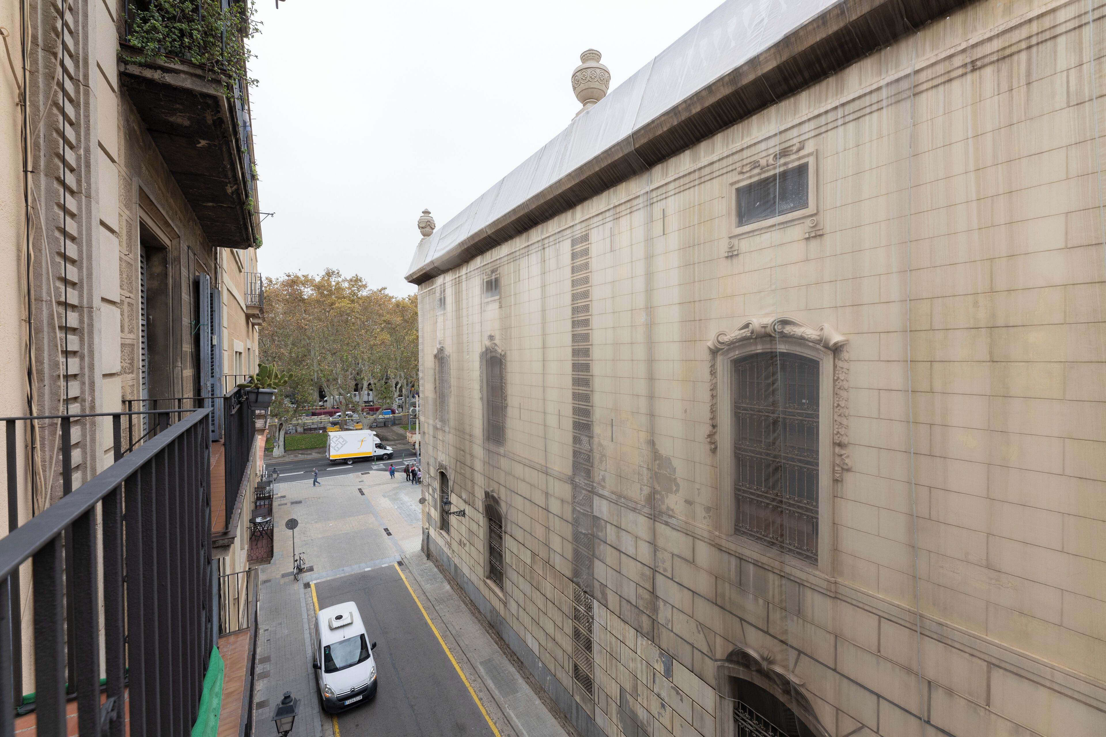 A narrow street with a white car parked on the side, buildings with classical architecture, and a green bike lane.