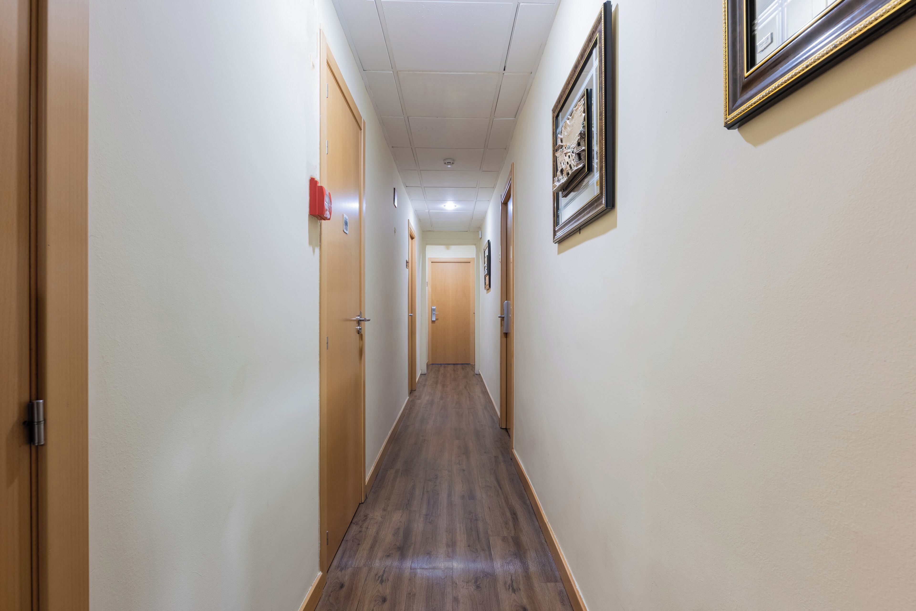 Un couloir étroit, doté d’un plancher en bois et de murs de couleur beige, qui mène à une porte au fond.