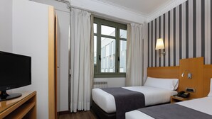Habitación de hotel con dos camas, un escritorio con ordenador, una ventana con cortinas y una pared a rayas.