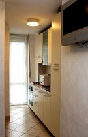 A narrow kitchen with white cabinets, a microwave, and a television mounted on the wall.