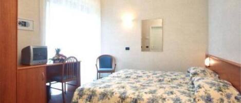 A hotel room with a bed, a desk with a computer, a chair, and a mirror on the wall.