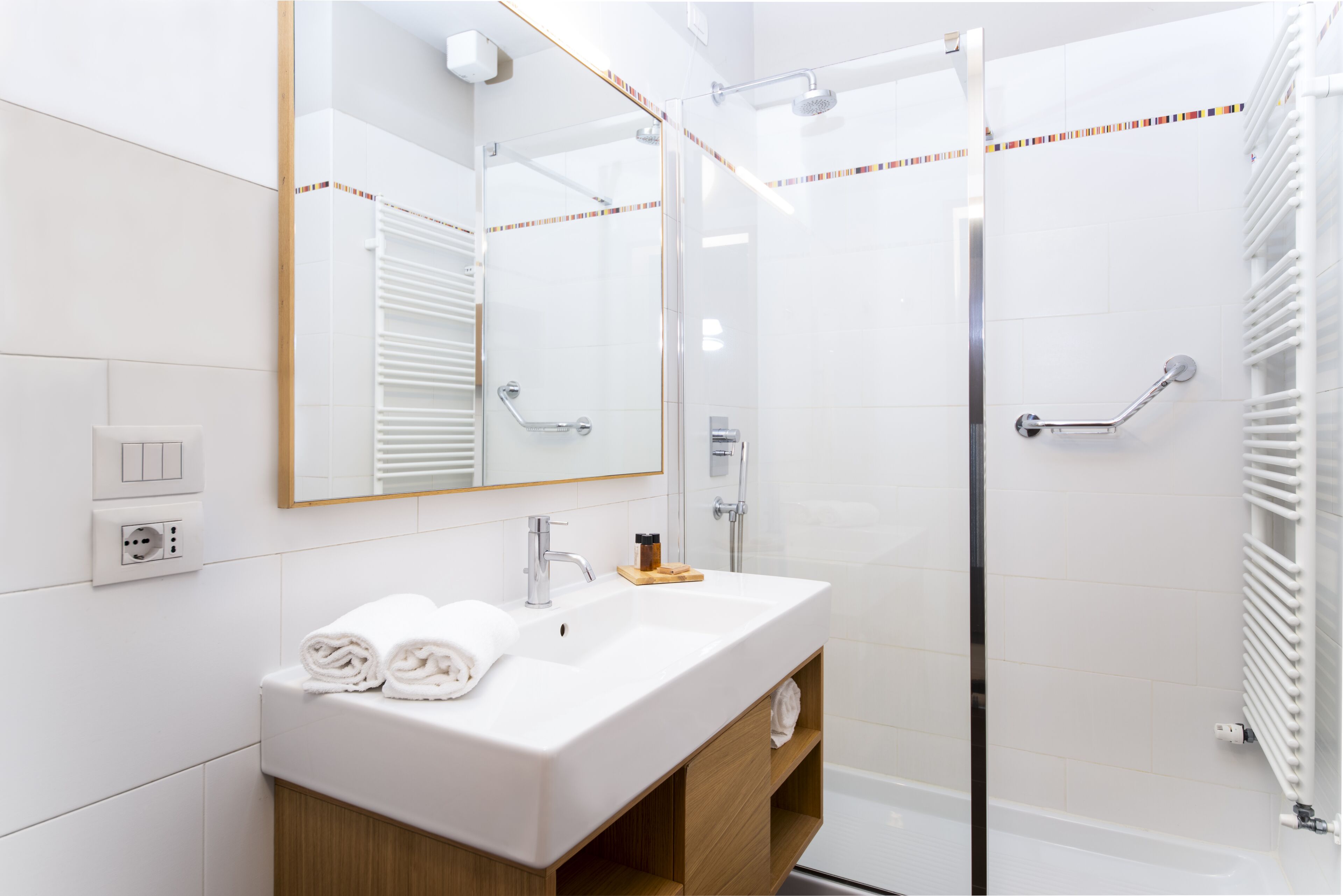 A modern bathroom with a white sink, mirror, and glass shower enclosure.
