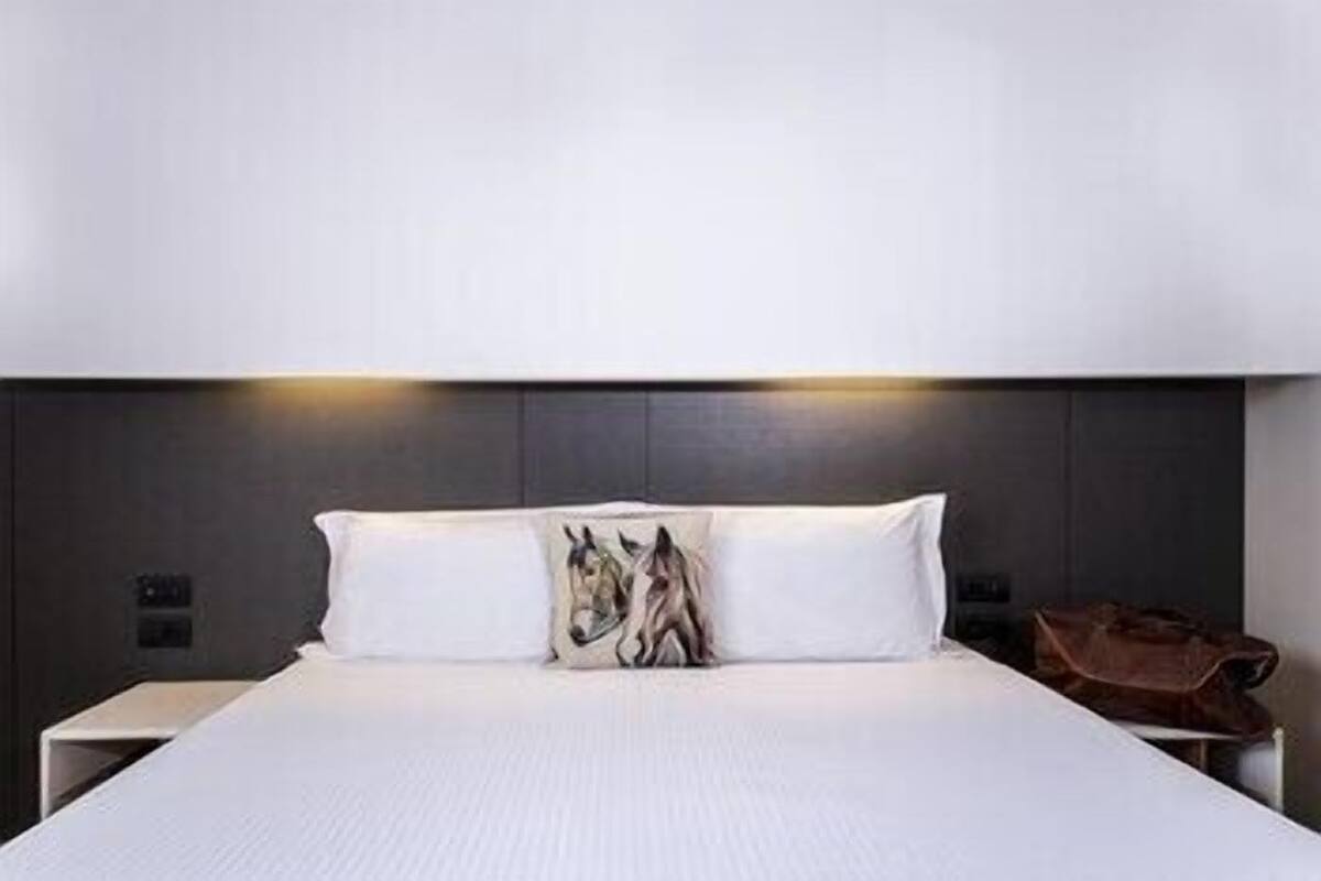 Een moderne hotelkamer met een groot bed, twee nachtkastjes en een hoofdeinde met ingebouwde verlichting.