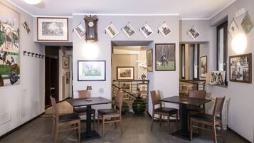 A dining area with tables and chairs, framed pictures on the walls, and a clock.
