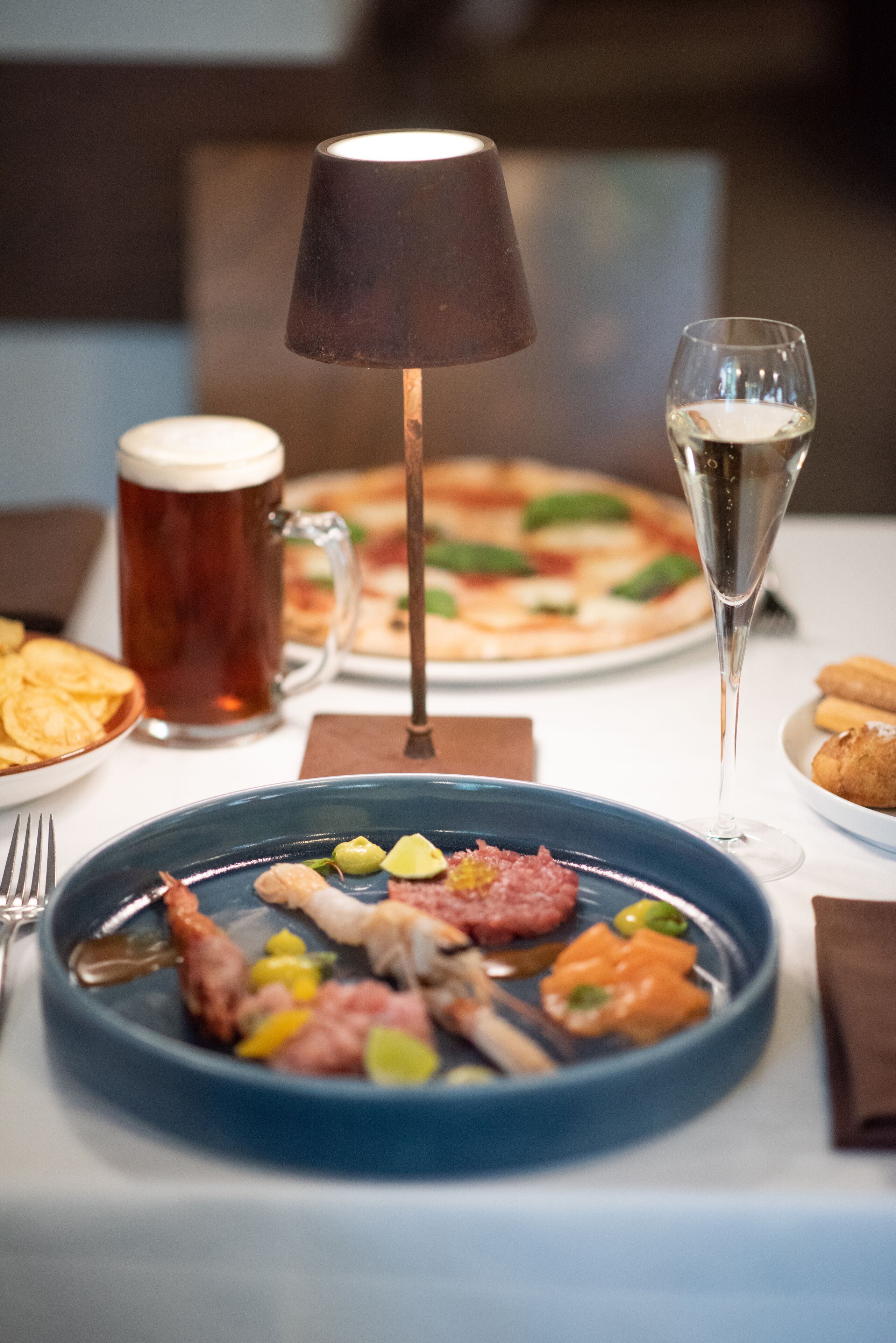 A dining table with a plate of food, a beer mug, a glass of wine, and a lamp.