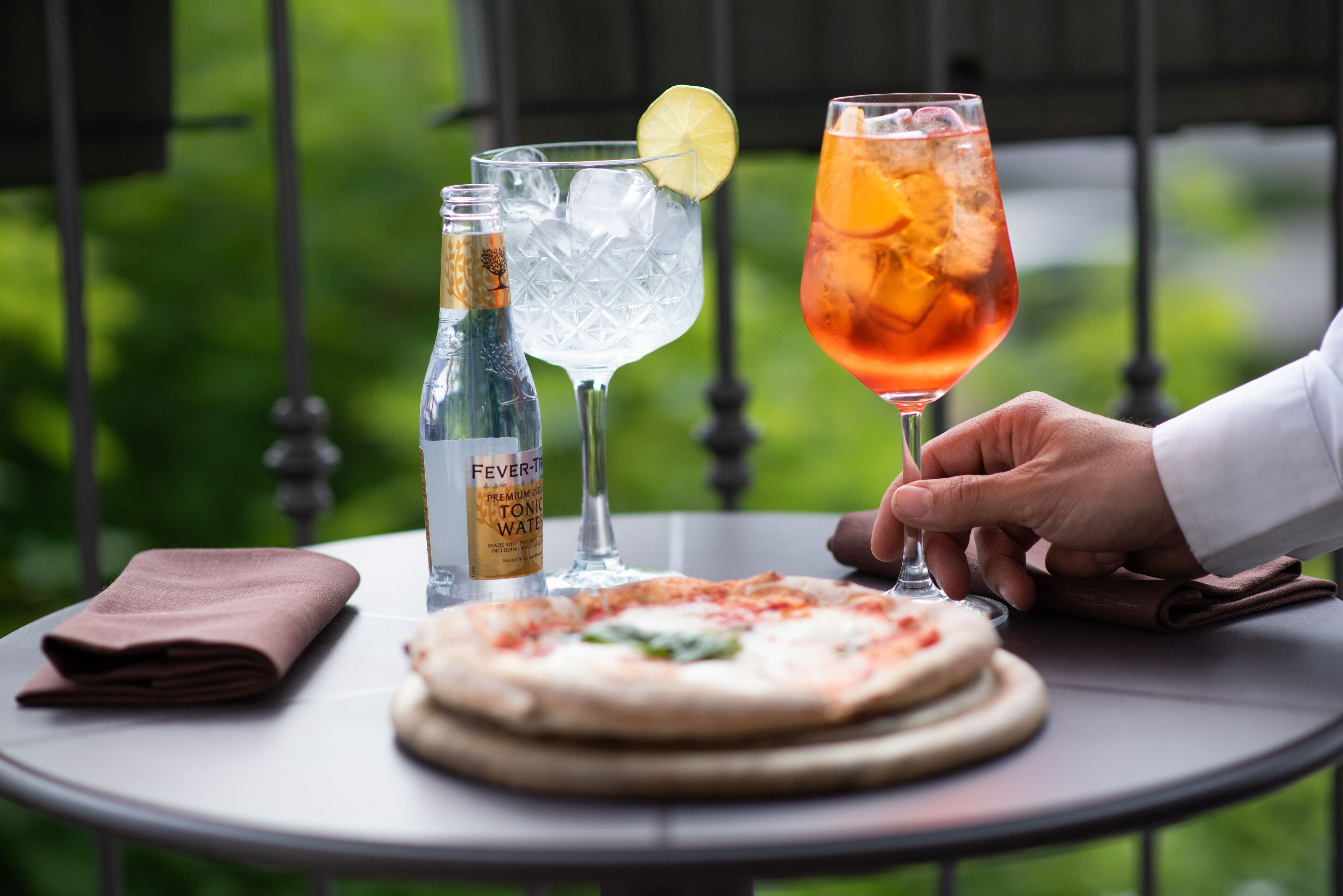 A table with a pizza, two drinks, and a bottle of water.