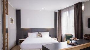 Ein modernes Hotelzimmer mit einem großen Bett, einem Schreibtisch, einem Sessel, einem Nachttisch und einem Kleiderschrank.
