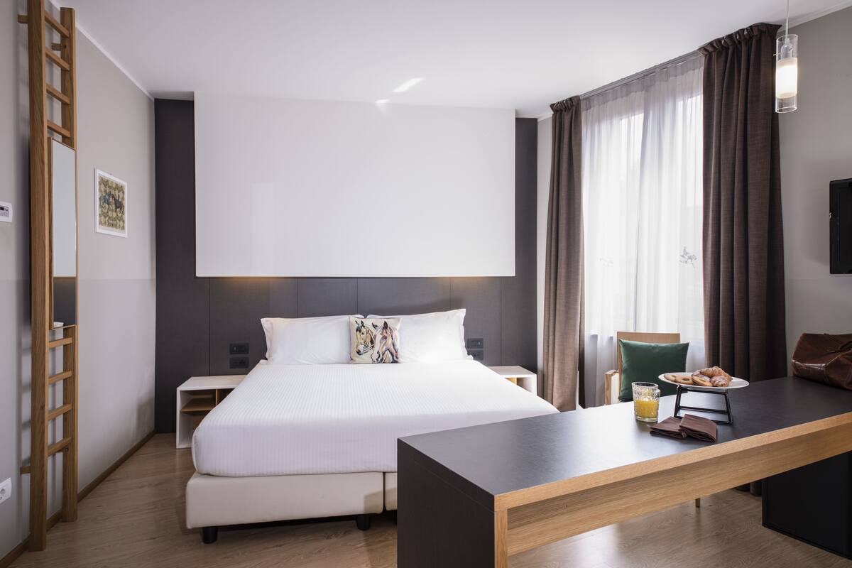 Een moderne hotelkamer met een groot bed, een bureau, een stoel, een nachtkastje en een garderobe.